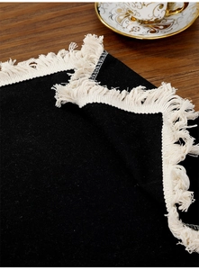 Detail of black cotton linen placemat with white fringe tassels on wooden table