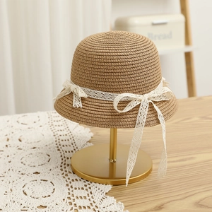 Detail of a khaki straw hat with white lace ribbon and bow on a golden display stand