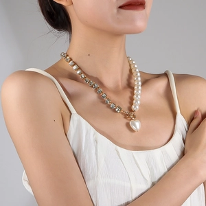 Close-up of asymmetric pearl necklace with heart pendant on a model in white dress