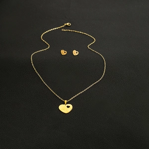 Detailed view of gold heart jewelry set with MOM engraving on black leather surface