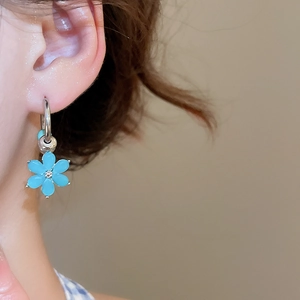 Detailed close-up of a silver hoop earring featuring a delicate blue flower-shaped pendant