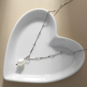Detail of a silver snake chain necklace with a pearl pendant on a white ceramic dish