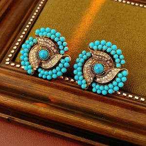 Vintage gold earrings with turquoise stones and crystals on a dark green fabric background