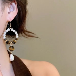 Close-up of model wearing tiger eye and pearl hoop earrings with drop pearl detail