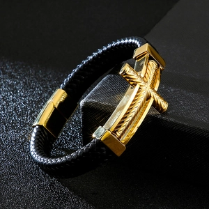 Close-up of golden metal cross with intricate textures on a braided black leather bracelet