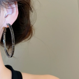 Close-up of large gunmetal hoop earrings with black zircon stones worn by a model