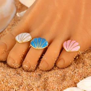 Three colorful shell toe rings in white blue and pink on a sunny beach background