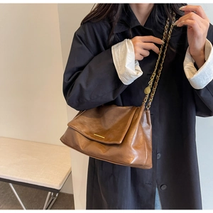 Detail of a brown leather shoulder bag featuring a gold metal bar and chain strap detail