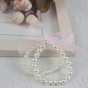 Close-up of white faux pearl bracelet with a pink mesh bow on a textured surface