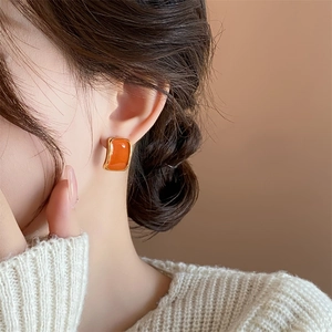 Close-up of elegant orange enamel square stud earring on model with golden frame