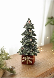 Miniature resin Christmas tree with golden gift box base and red berries on wood desk