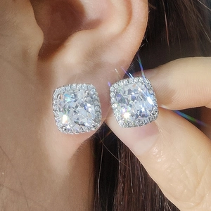 Macro shot of sparkling square-cut zircon halo earrings with silver setting on ear
