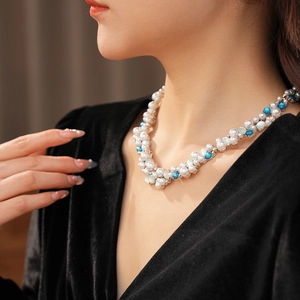Dettaglio di una collana vintage con perle bianche e perline turchesi indossata dal modello