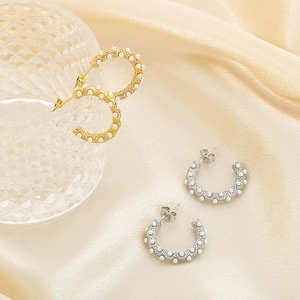 Detailed view of gold and silver C-shaped pearl earrings on silk fabric background