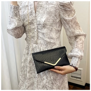 Détail du sac enveloppe plissé noir avec décor V doré et bandoulière chaîne