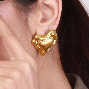 Gros plan d'une boucle d'oreille cœur en or avec texture de métal liquide sur l'oreille