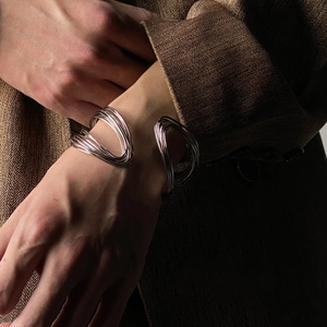 Detail of silver twisted multilayer open cuff bracelet worn with a brown blazer