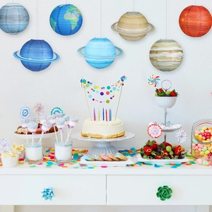 Solar system planet paper lanterns hanging over a colorful birthday party dessert table