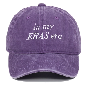 Detailed close-up of white 'in my ERAS era' embroidery on a washed purple cotton baseball cap