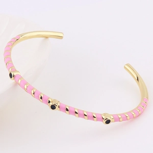 Detail of gold-plated bangle featuring pink enamel stripes and black circular accents