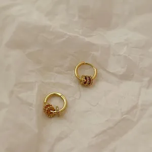 Close-up of gold hoop earrings with zircon studded charms on textured paper