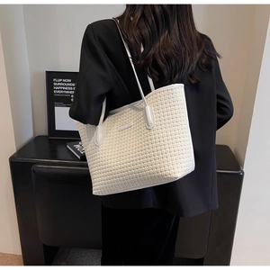 Modern white woven tote bag with slim shoulder straps worn over a black blazer jacket