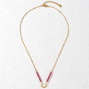 Close-up of gold titanium steel beaded necklace with red beads and crescent pendant