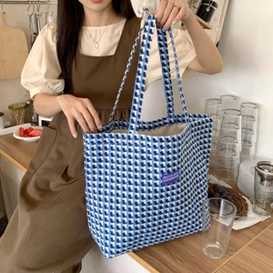 Blue and white plaid woven tote bag with a purple label being held by a model