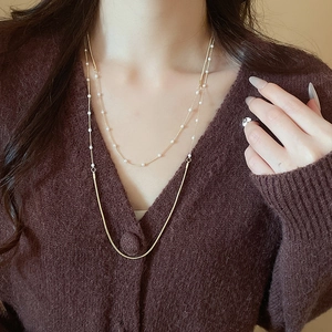 Close-up of layered gold snake chain and pearl necklace worn on a brown cardigan
