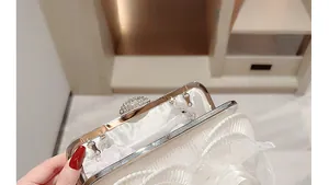 Close-up of white satin bridal clutch with pleated fabric, 3D floral accent and rhinestone clasp