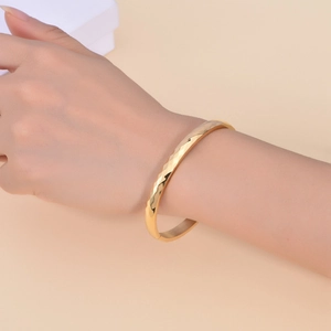 Detail of gold titanium steel bangle showing geometric diamond-cut facets on wrist