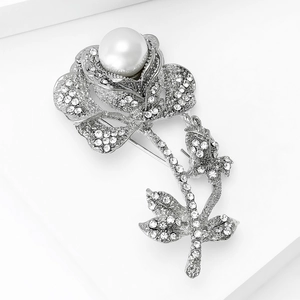 Detailed shot of a silver rose brooch featuring clear rhinestones and a white pearl