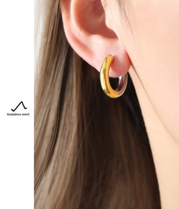 Detailed view of polished gold plated stainless steel hoop earring worn by a model