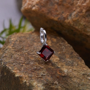 Macro shot of an S925 silver pendant with a square red gemstone on a textured rock