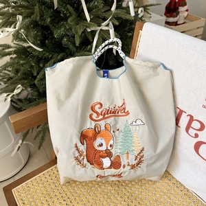 Close-up of squirrel and pine embroidery on a beige nylon tote bag with rope handle