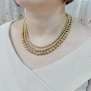 Detailed close-up of a triple layered 18K gold bead necklace on a female model