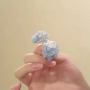 Macro shot of hand-woven beaded flower stud earrings in light blue and white color