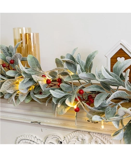 Detail of Christmas garland with frosted leaves, red berries and warm LED lights
