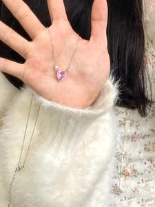 Detailed view of a pink heart-shaped crystal necklace held by hand on a soft background