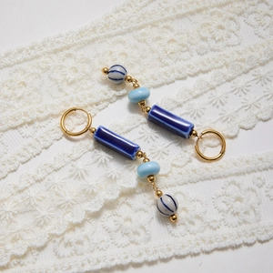 Detail of vintage blue ceramic tassel earrings with golden hooks on white lace background