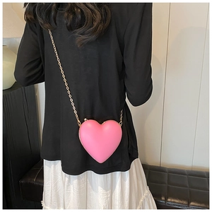 Rear view of a pink heart-shaped crossbody bag with a gold chain strap on a black outfit