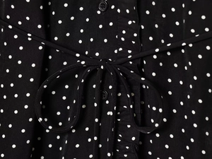 Detail of black polka dot dress featuring a front tie bow and matching black buttons