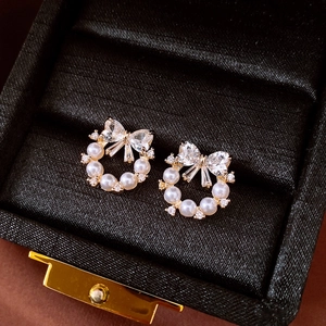 Macro shot of bowknot earrings with white pearls and zircons on black velvet box