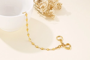 Detailed shot of golden heart-link bracelet with T-bar clasp on ceramic bowl decor