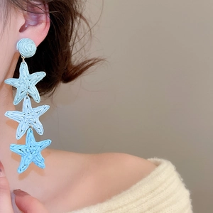Detail of blue raffia star tassel earrings worn by a model in a resort vacation style