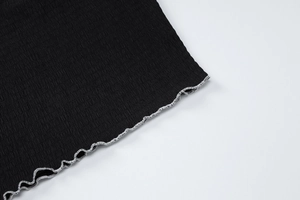 Détail du tissu plissé noir avec ourlet à bord ondulé et texture à fines côtes