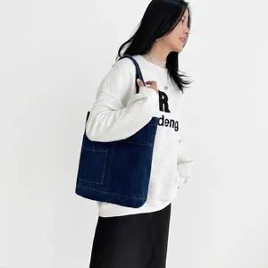 Detail of blue denim tote bag with large front pocket styled on a female model
