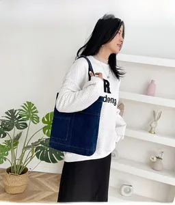 Dettaglio di borsa tote in denim blu con grande tasca frontale indossata da una modella