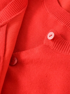 Close-up of red knit jacket featuring ribbed collar and matching satin sheen buttons