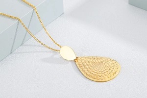 Macro detail of golden teardrop pendant with embossed dot texture and smooth metal oval
